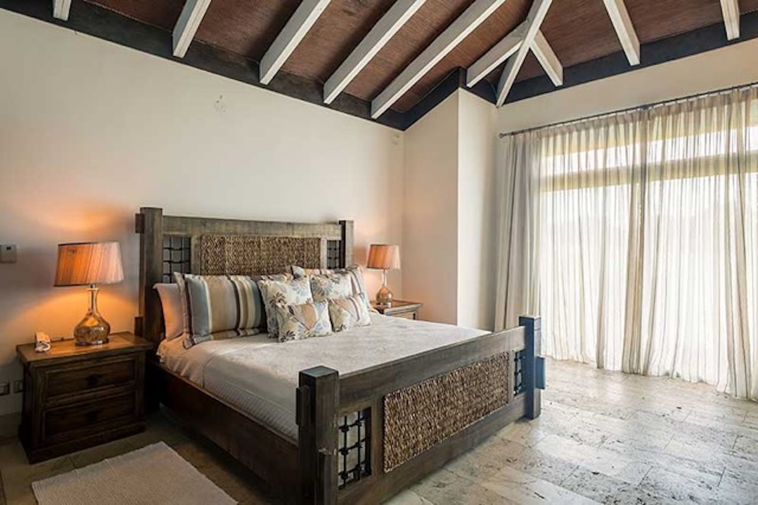 A bedroom with a wooden bed, two bedside tables, and a large window with curtains.