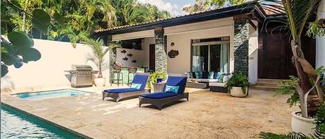 Un área junto a la piscina con sillones de descanso, un pequeño patio y una piscina.