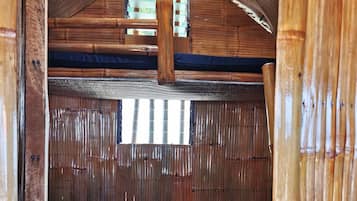 A wooden interior with a sloped ceiling, a window with a view, and a bed with a dark mattress.