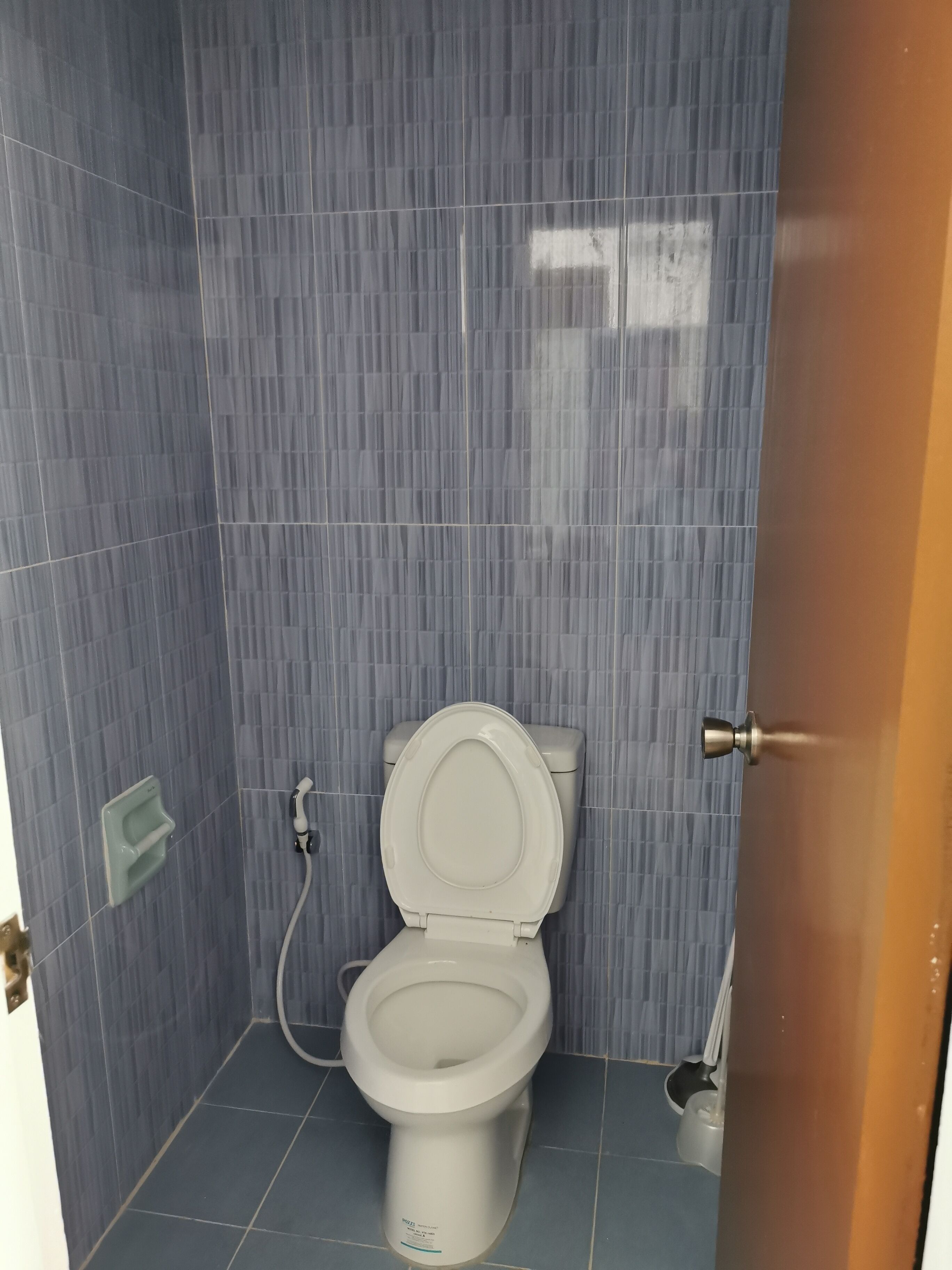 Un bany petit i compacte amb un vàter, un assecador de mans i un dispensador de paper higiènic fixat a la paret.