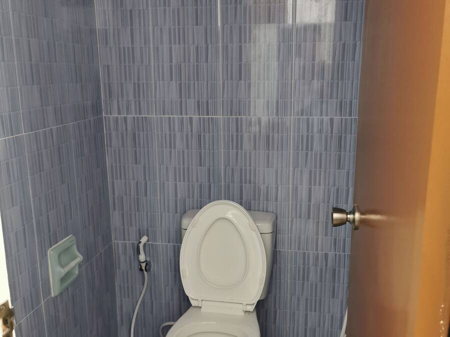 Un bany petit i compacte amb un vàter, un assecador de mans i un dispensador de paper higiènic fixat a la paret.