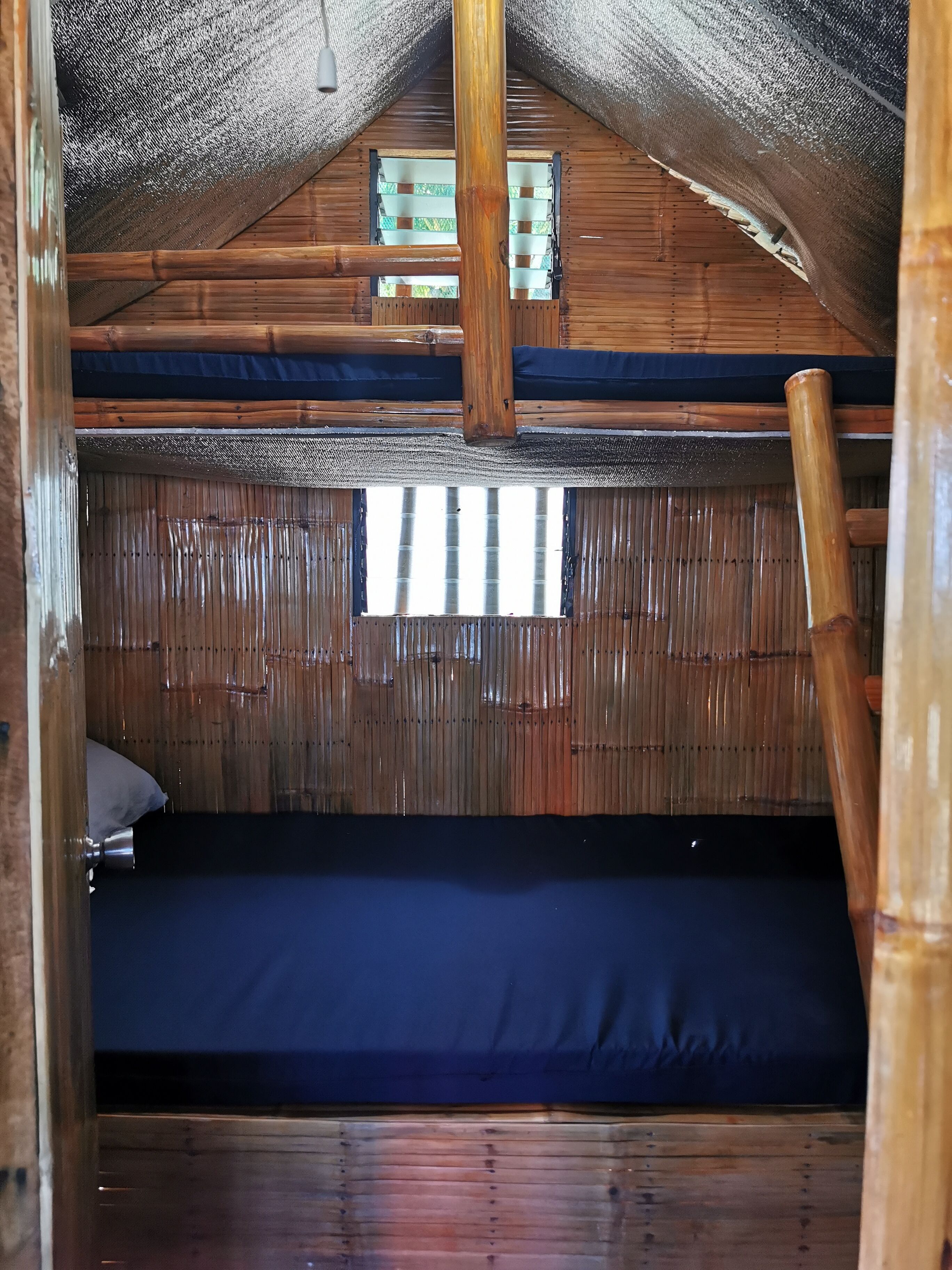 A wooden cabin interior with a bunk bed, a window with a view, and a ladder.