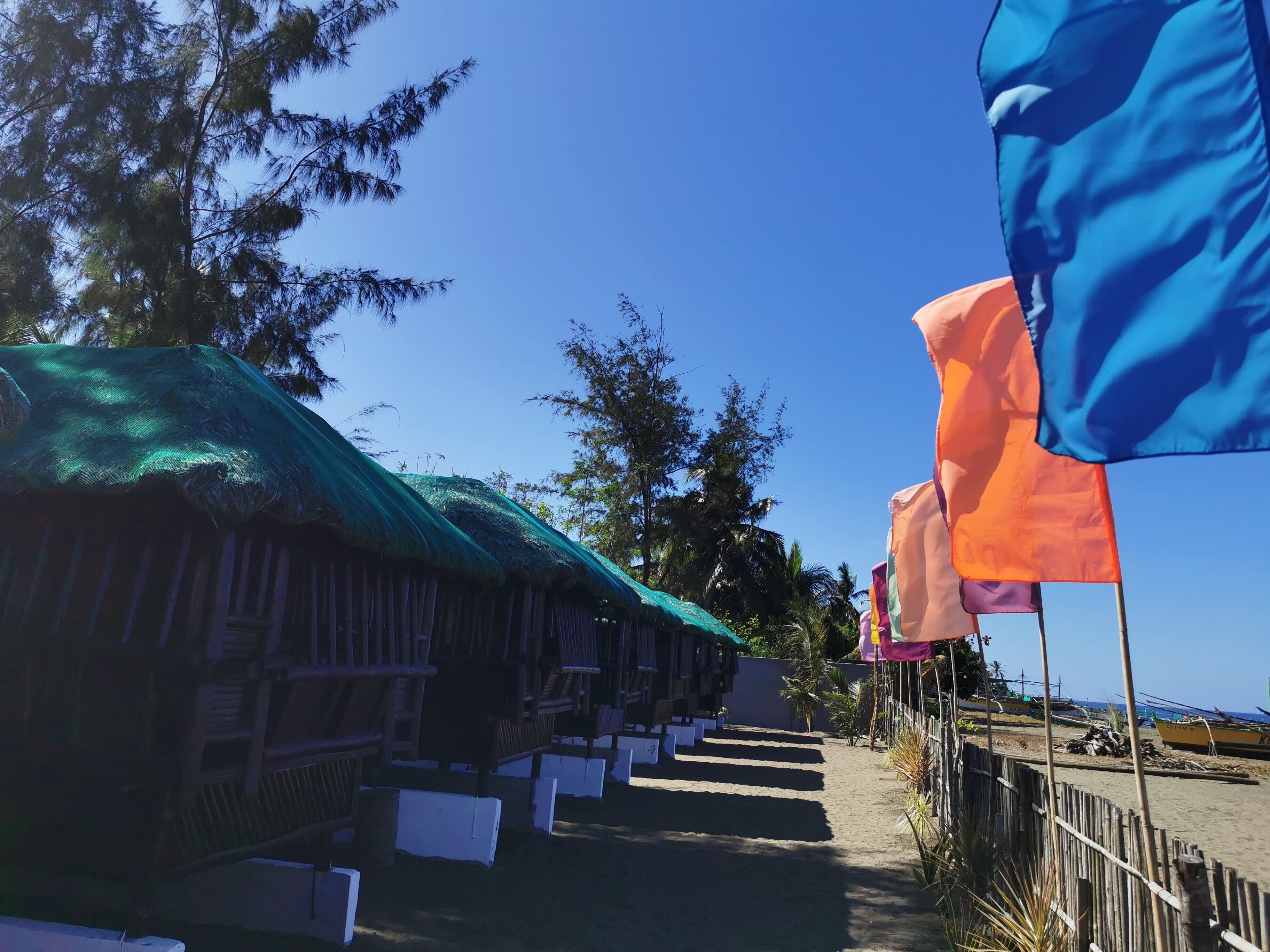 A row of thatched-roof huts with a sandy path leading to the beach.