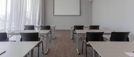 A conference room with a large screen, six tables, and chairs arranged for meetings.