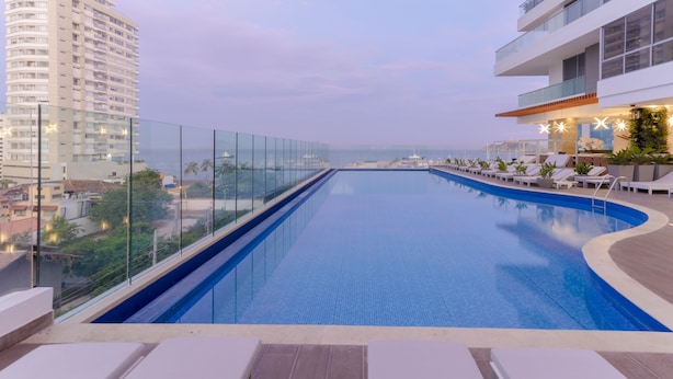 A rooftop infinity pool with lounge chairs, a glass railing, and a view of the cityscape. - AC Hotel by Marriott Santa Marta (Santa Marta)