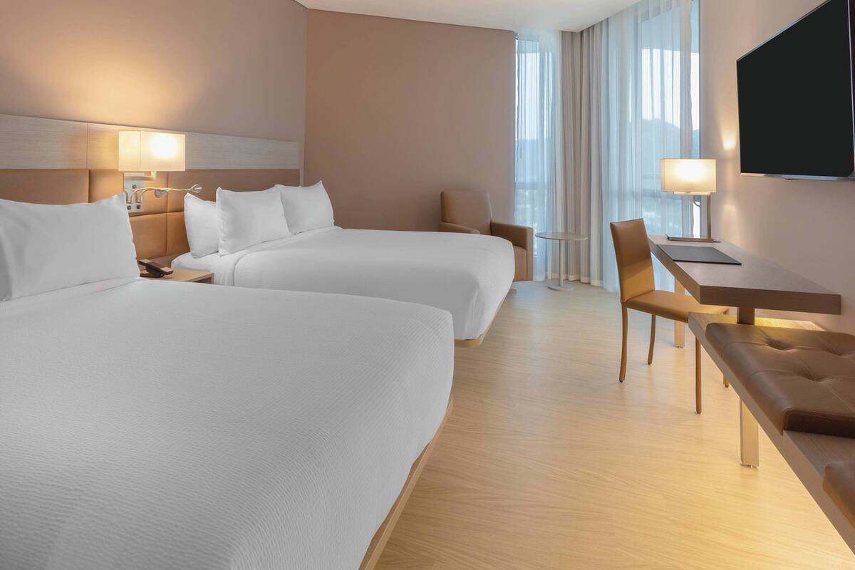 Una habitación de hotel con dos camas, un escritorio, una silla y un televisor.