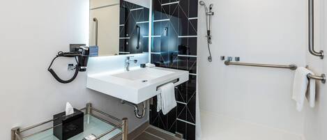 A modern bathroom with a glass-topped vanity, a white sink, a large mirror, and a black tiled shower area.