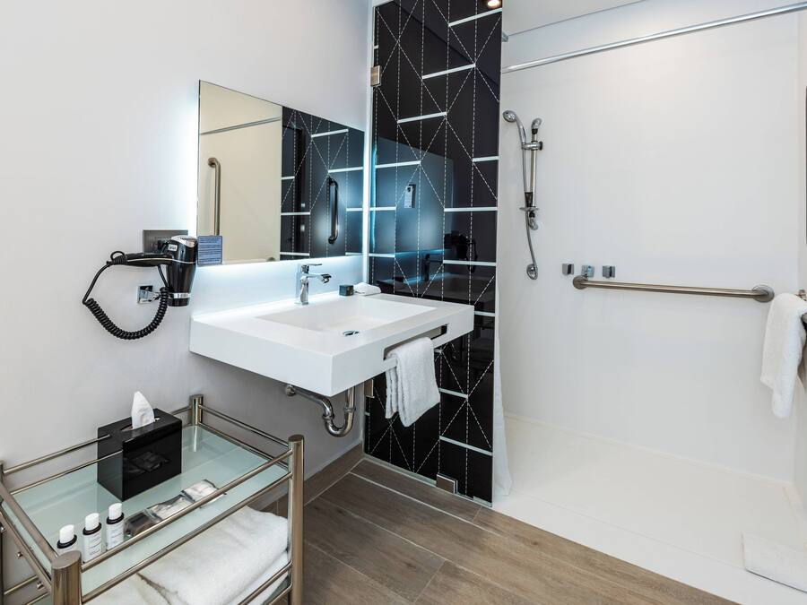 A modern bathroom with a glass-topped vanity, a white sink, a large mirror, and a black tiled shower area.