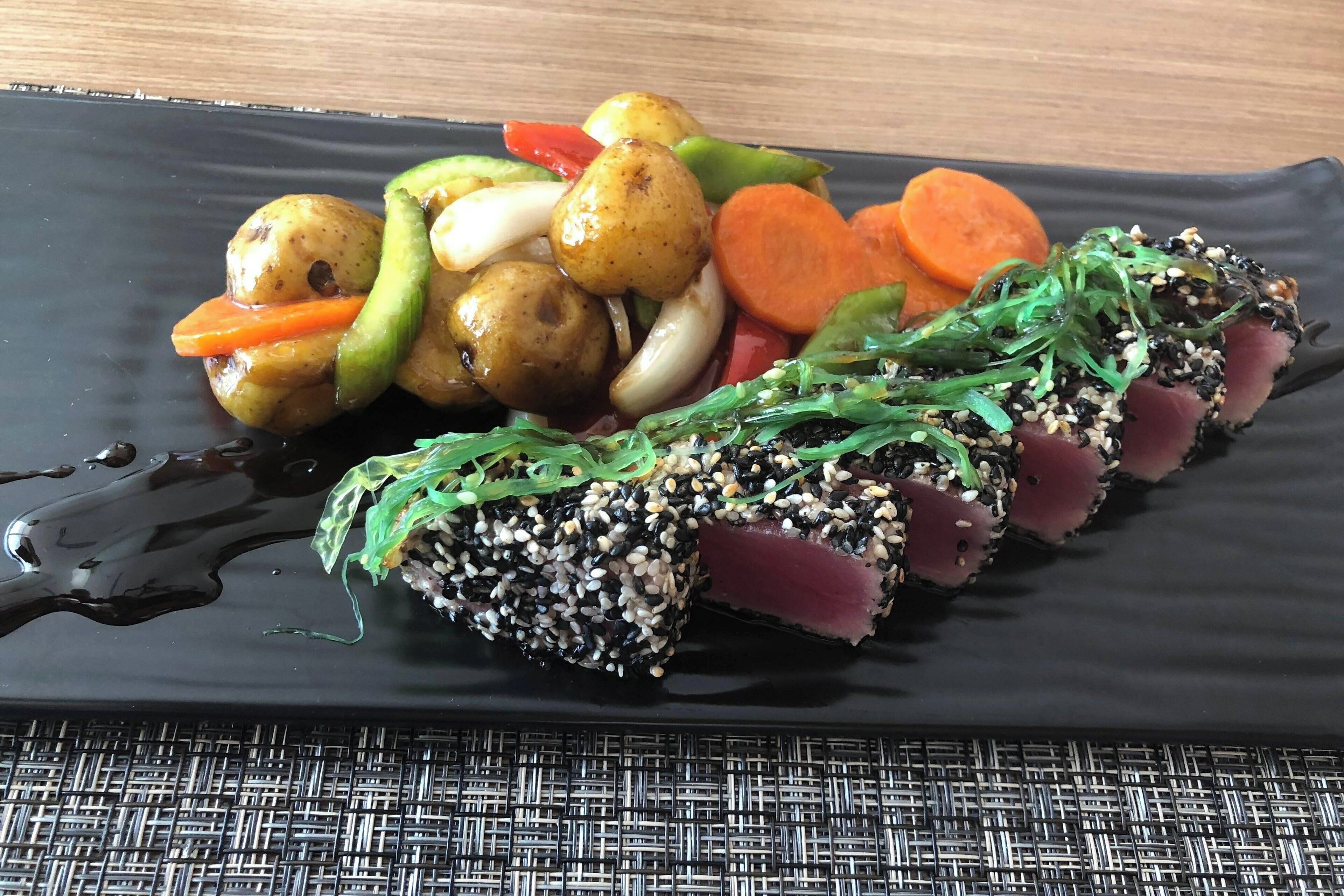A black plate with a dish of seared tuna, vegetables, and a sauce.