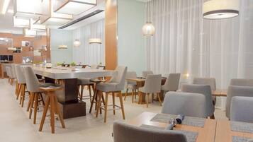 Un comedor moderno con una larga mesa común, mesas individuales y sillas.
