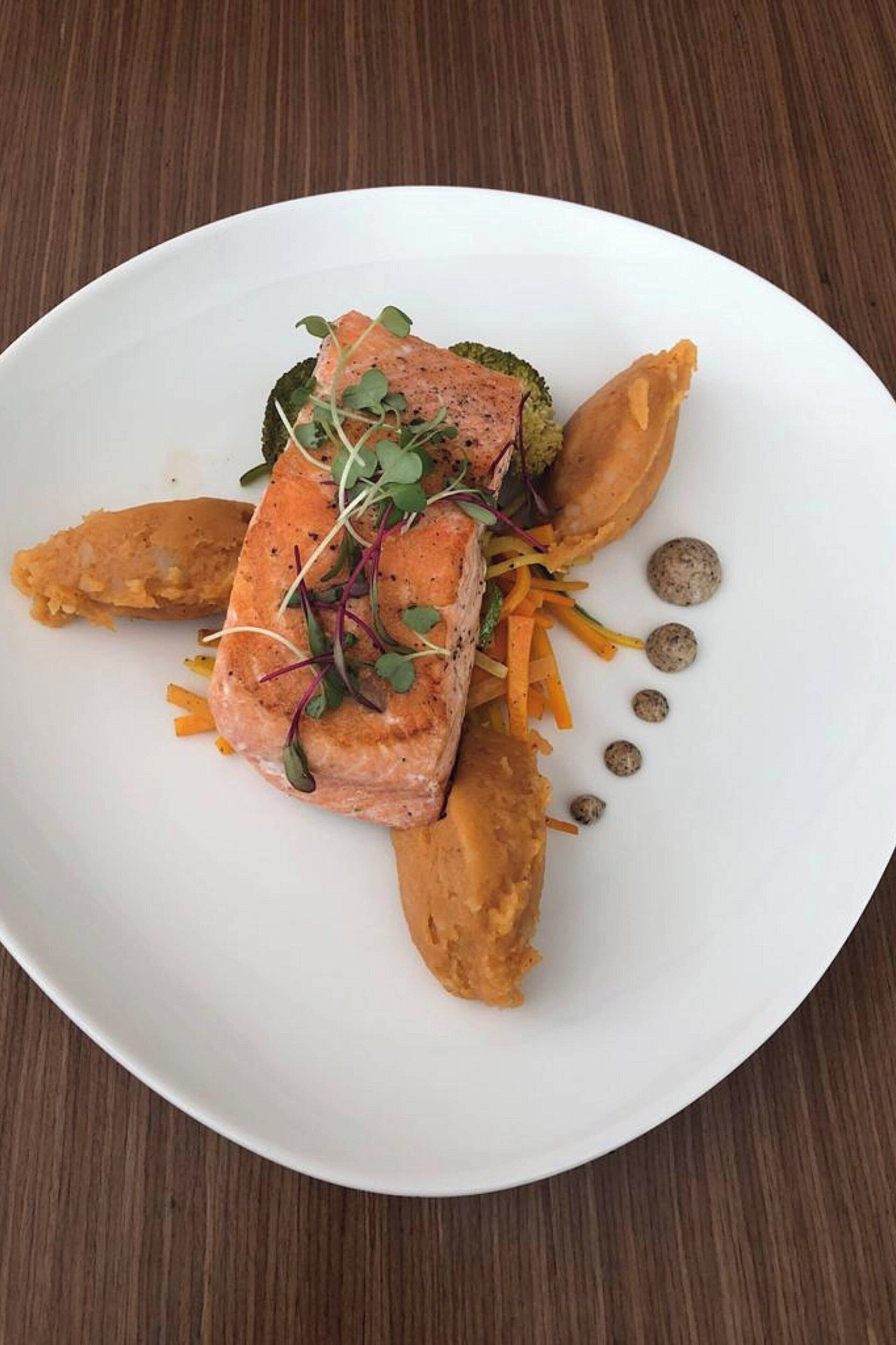 A white plate with a piece of salmon, a vegetable, and some garnishes.
