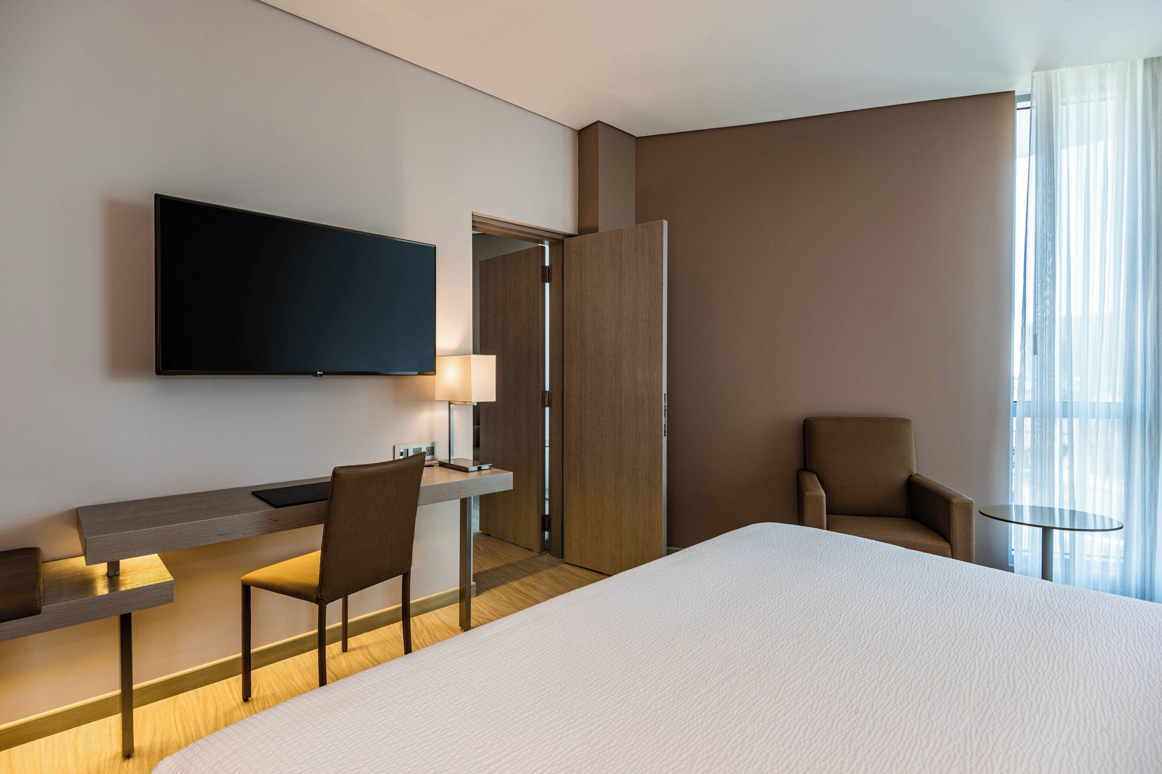 Una habitación de hotel con una cama grande, un escritorio con silla, televisión y una ventana con cortinas.