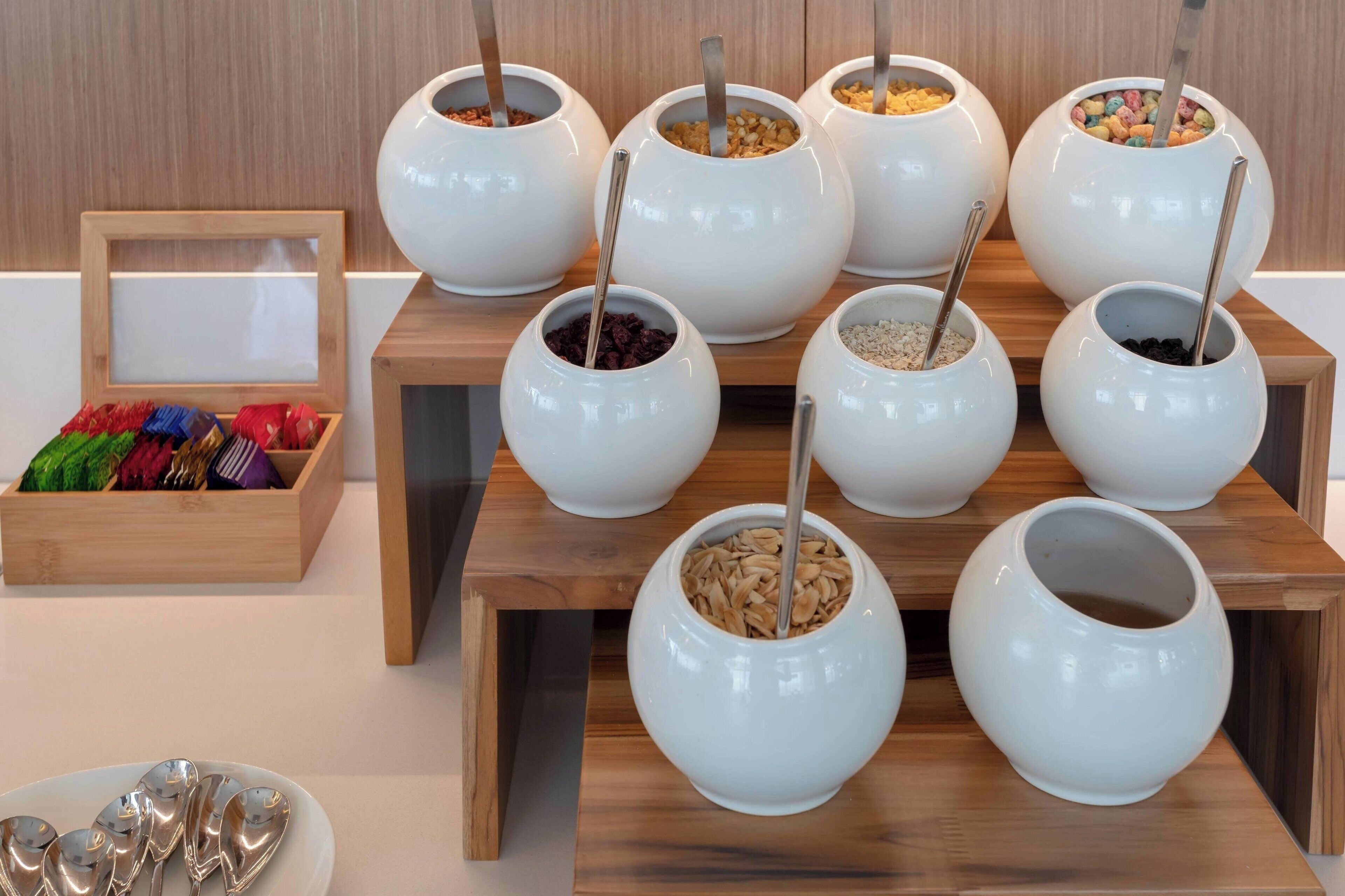 Un buffet avec des plats blancs contenant différents types d’aliments, chacun accompagné d’une cuillère.