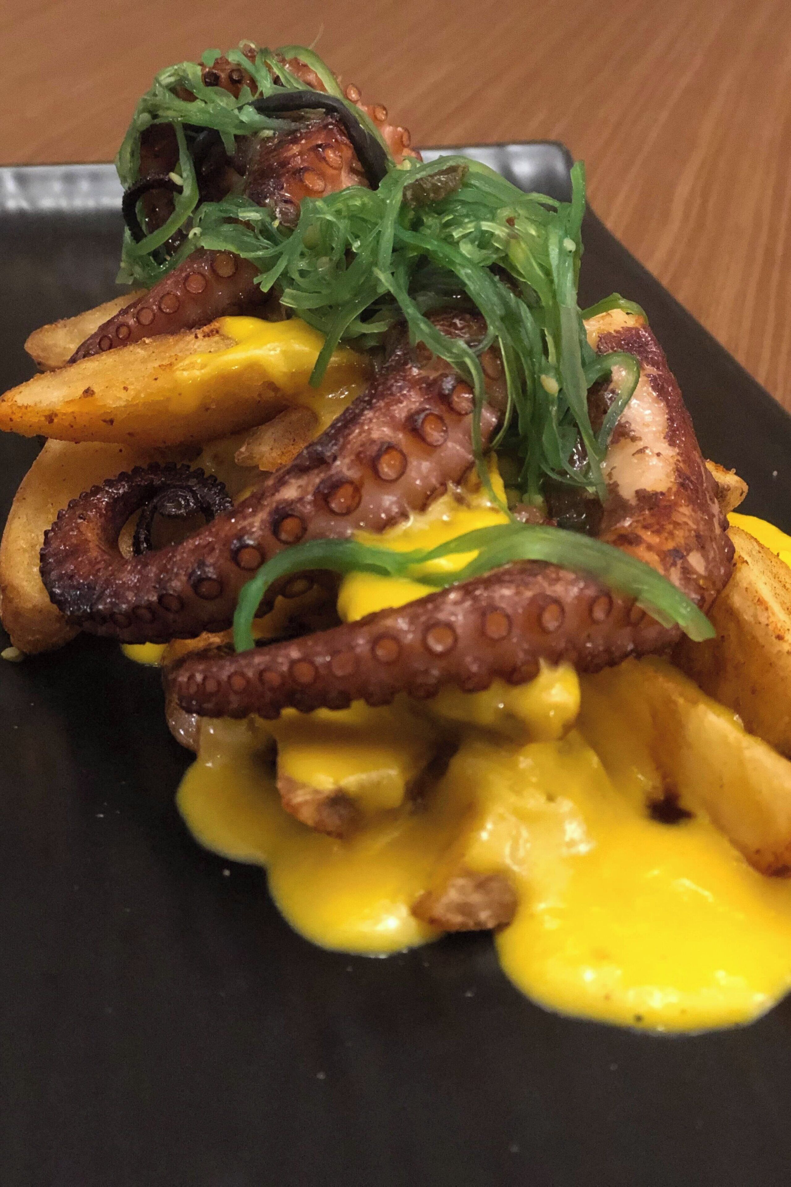 A dish of grilled octopus with potatoes and a yellow sauce.