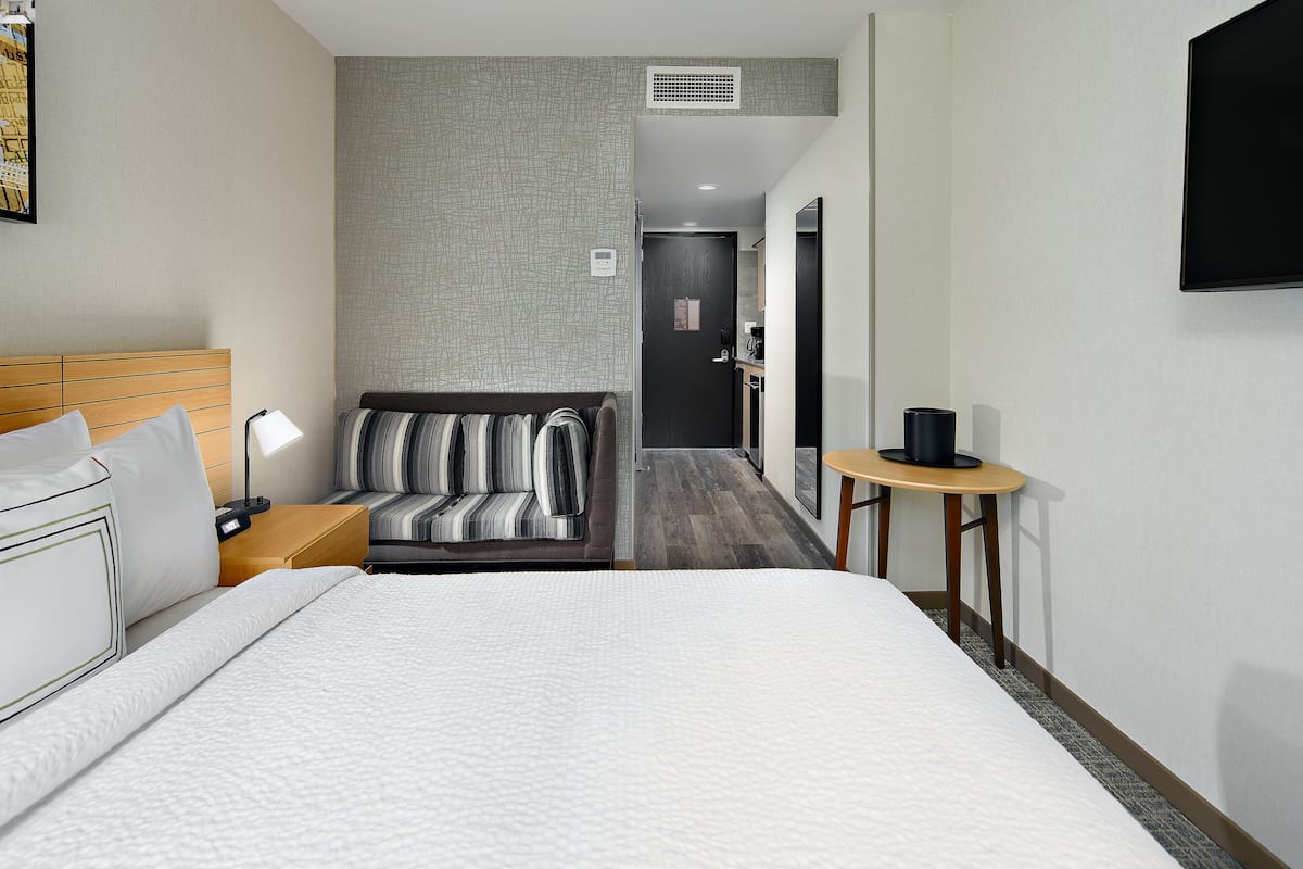 A hotel room with a large bed, a sofa, a small table, and a TV.