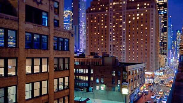 A nighttime cityscape with tall buildings, some with illuminated windows and signage.