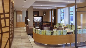 A modern hotel lobby with a curved reception desk, seating area, and a television.