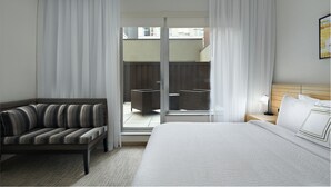 A hotel room with a bed, a sofa, a nightstand, and a view of the outside balcony.