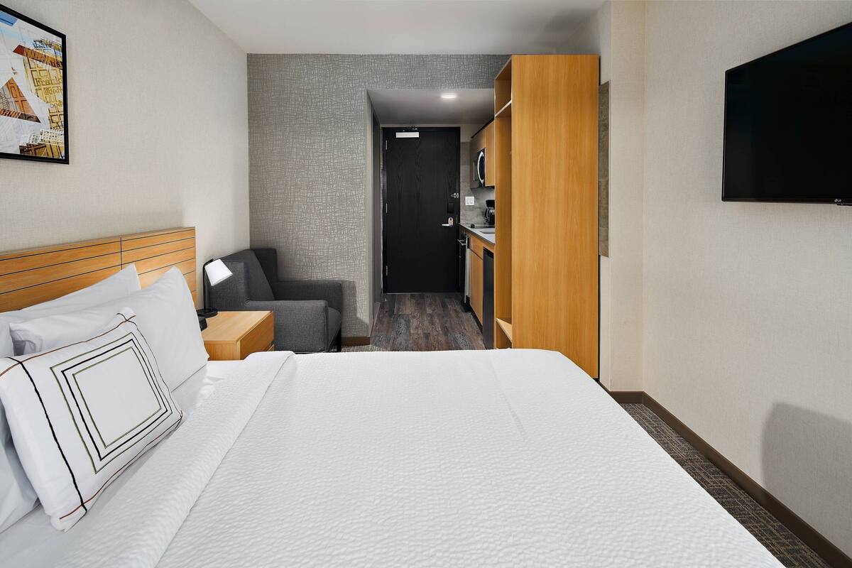 A hotel room with a large bed, a desk, a chair, a television, and a wardrobe.