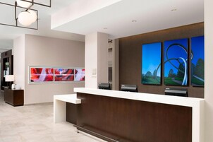 A modern reception area with a white reception desk, a large digital screen displaying colorful images, and three framed landscape paintings on the wall.