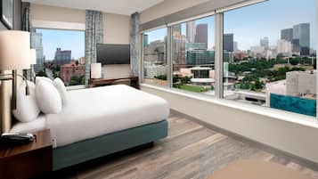 Habitación de hotel con una cama grande, televisor y vista a la ciudad.