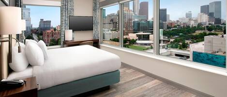 Habitación de hotel con una cama grande, televisor y vista a la ciudad.