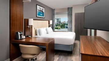 A hotel room with a bed, desk, chair, and a television.