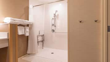 A modern bathroom with a walk-in shower, a wooden vanity with a mirror, and a towel rack with folded towels.