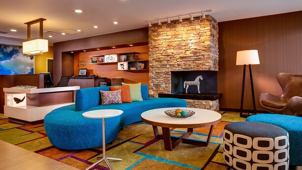 A modern hotel lobby with a stone fireplace, a blue sofa, a round table, and a reception desk. - Fairfield Inn & Suites by Marriott Somerset (Somerset)