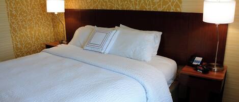 A hotel room with a neatly made bed, two bedside lamps, a bedside phone, and a patterned wallpaper.