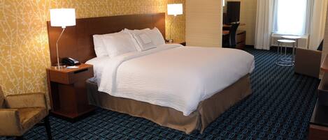 A hotel room with a large bed, two bedside lamps, a desk with a chair, and a small table.