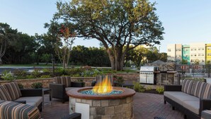 Un patio al aire libre con un hogar de piedra, muebles de mimbre y vista a un edificio en el fondo.
