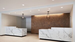 Uma área de recepção moderna, com balcões de mármore, iluminação embutida no teto e uma parede de madeira com textura.