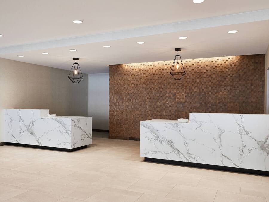 A modern reception area with marble reception desks, recessed ceiling lighting, and a textured wooden wall.