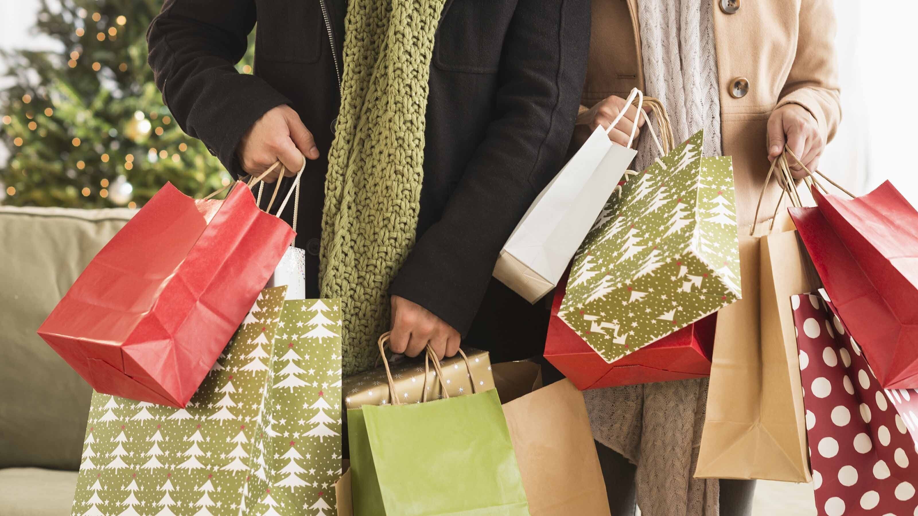 Une personne tenant plusieurs sacs de courses décorés sur le thème de Noël.