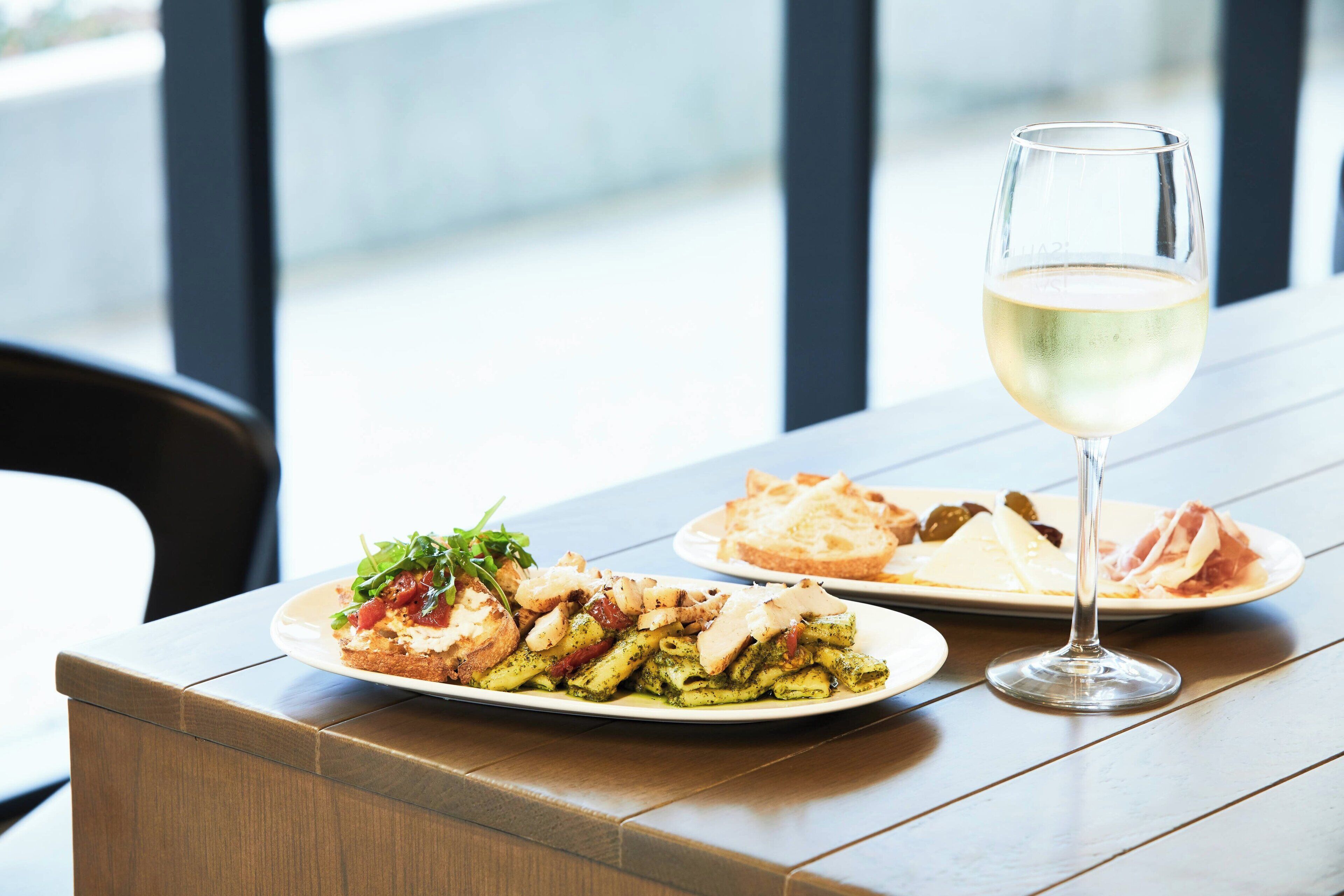 A table with two plates of food and a glass of white wine.