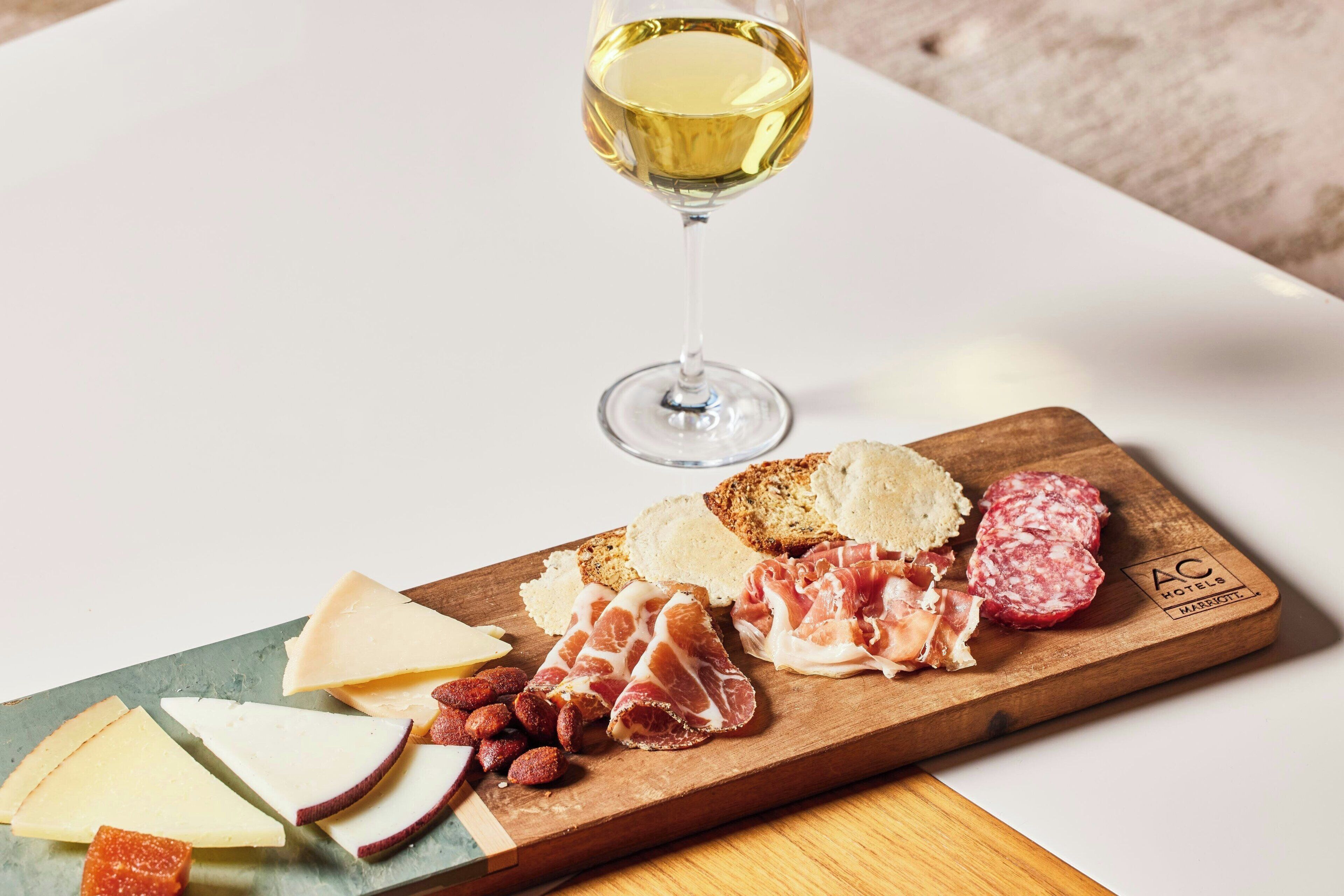 A wooden board with various cheeses, cured meats, and bread, accompanied by a glass of white wine.
