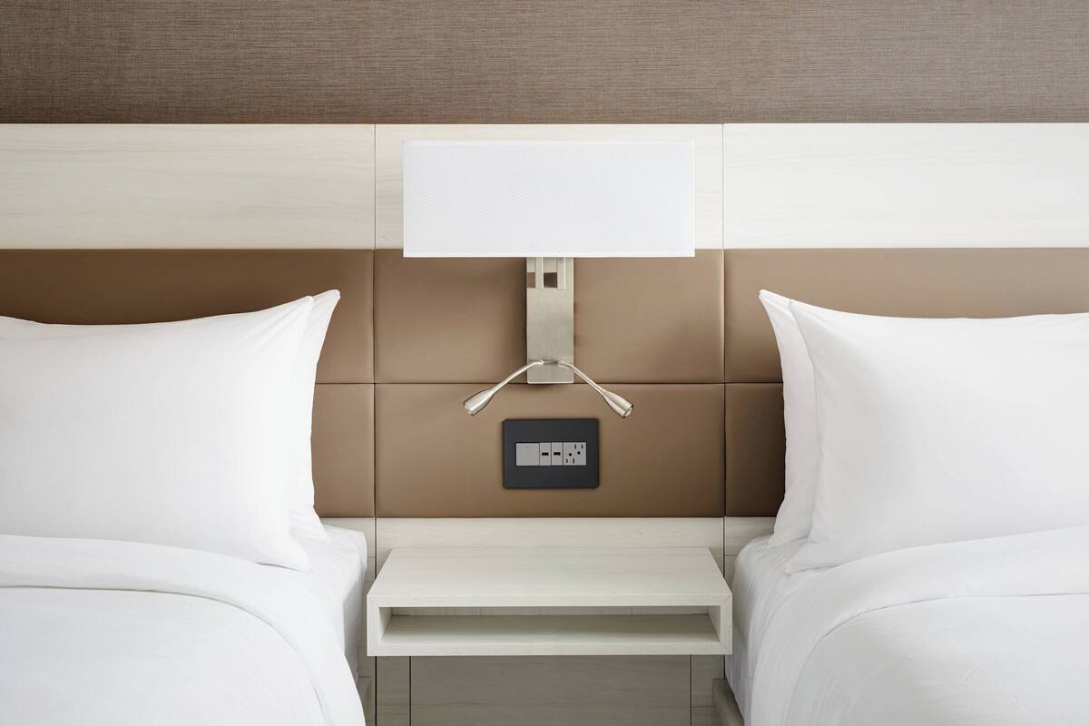 Een hotelkamer met een bed, nachtkastjes, een lampje aan de muur en een stopcontact.