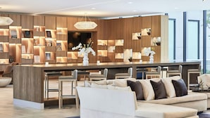 A modern hotel lobby with a central bar area, seating arrangements, and a large window providing natural light. - AC Hotel by Marriott Dallas by the Galleria (Dallas)