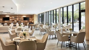 A modern hotel lobby with a spacious seating area, a bar, and large windows offering a view of the outdoors. - AC Hotel by Marriott Dallas by the Galleria (Dallas)