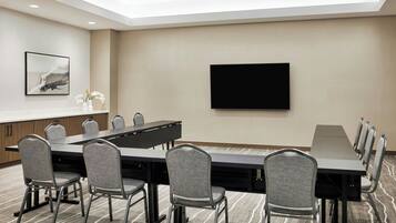 A conference room with a long table, six chairs, a flat-screen TV, and a framed artwork on the wall.
