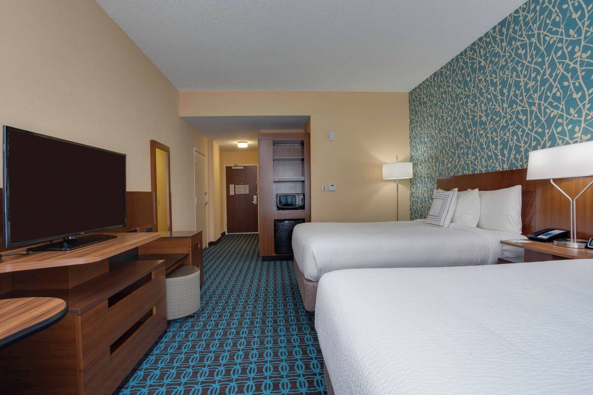 Une chambre d’hôtel avec deux lits, une télévision, un bureau et une salle de bain visible à travers une porte ouverte.