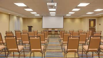 A conference room with rows of chairs, a projector screen, and a carpeted floor.