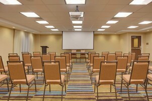 A conference room with rows of chairs, a projector screen, and a carpeted floor.