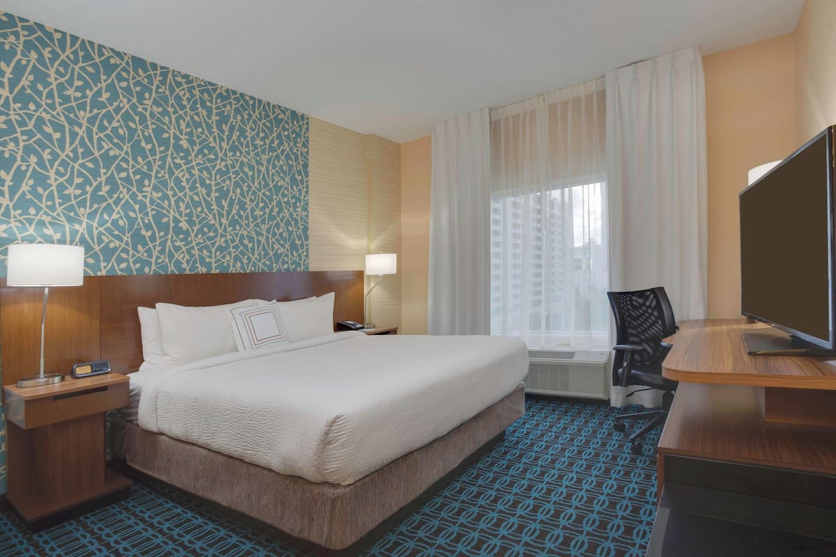 Une chambre d’hôtel avec un grand lit, des lampes de chevet, un bureau avec un ordinateur, une chaise et un téléviseur.