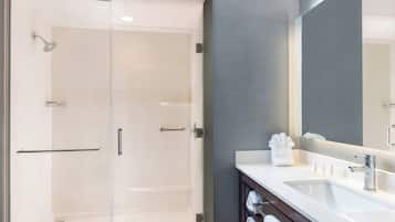 Une salle de bain moderne avec une douche à parois de verre, un lavabo blanc avec un grand miroir et des serviettes soigneusement rangées.
