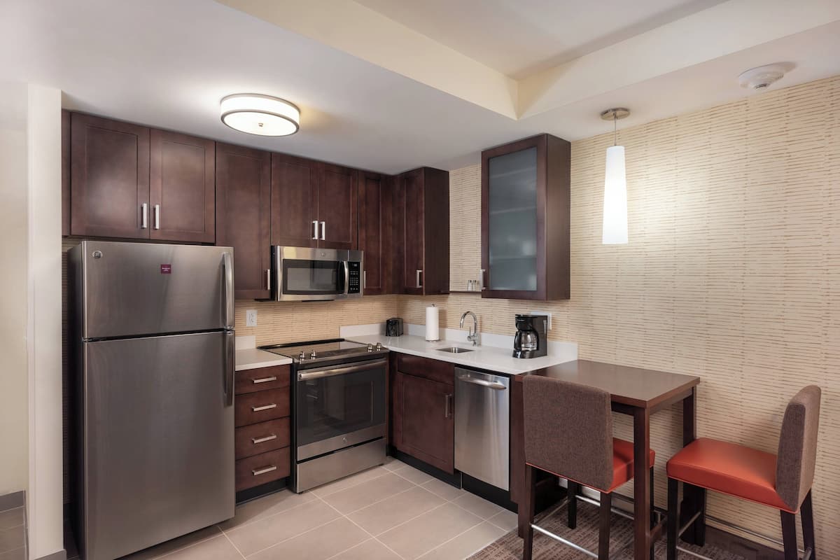 A compact kitchen with dark wooden cabinets, stainless steel appliances, a microwave, and a small dining area with a table and two chairs.
