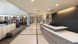 A hotel reception area with a long reception desk, seating area, and a hallway leading to other rooms. - Residence Inn by Marriott Greenville (Greenville)