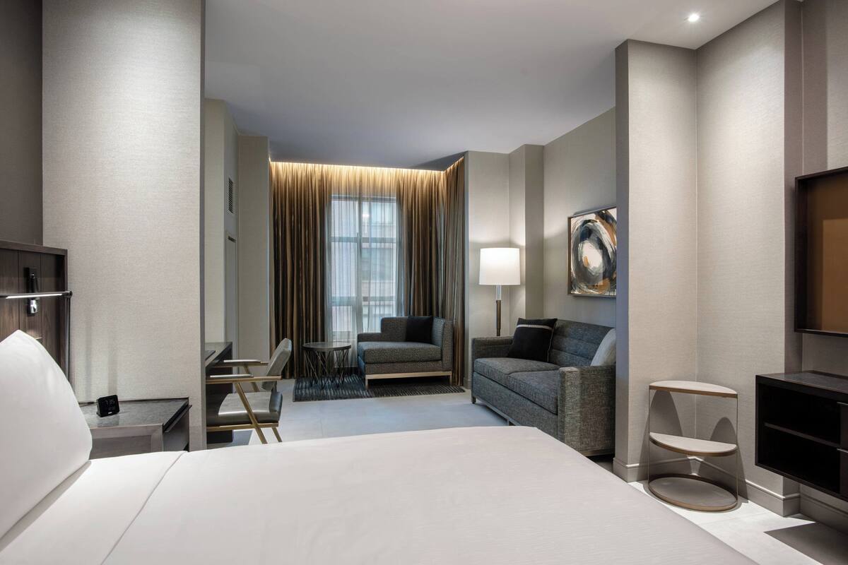 Ein modernes Hotelzimmer mit einem großen Bett, einer Couch, einem kleinen Tisch und einem Fernseher.
