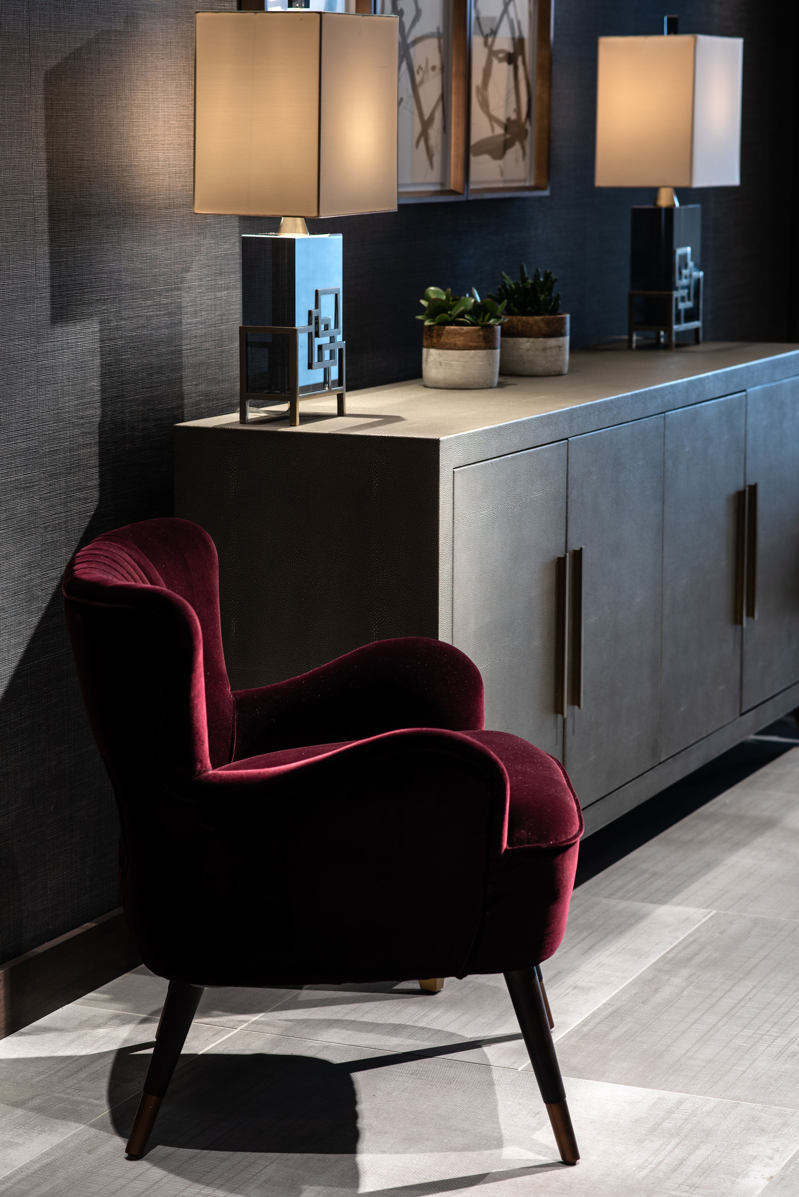 A modern room with a dark grey cabinet, a red velvet chair, and two floor lamps.